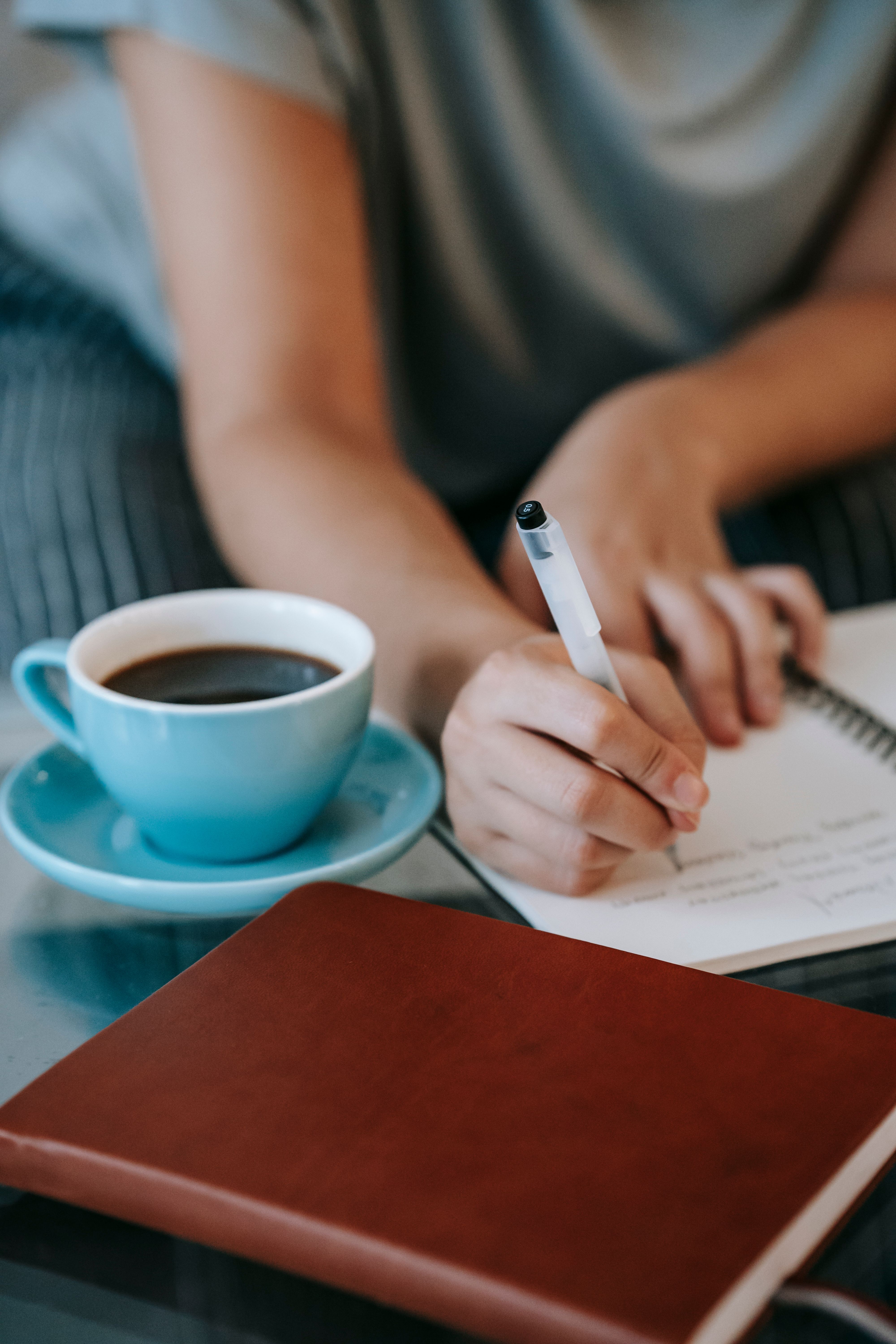 Žena zapisuje plan u bilježnicu uz šolju kafe, editorial fotografija za članak o finansijskoj sigurnosti.